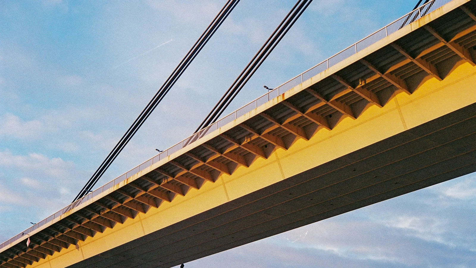 Estrutura e cabos de uma ponte amarela sobre o rio, fotografados de baixo.