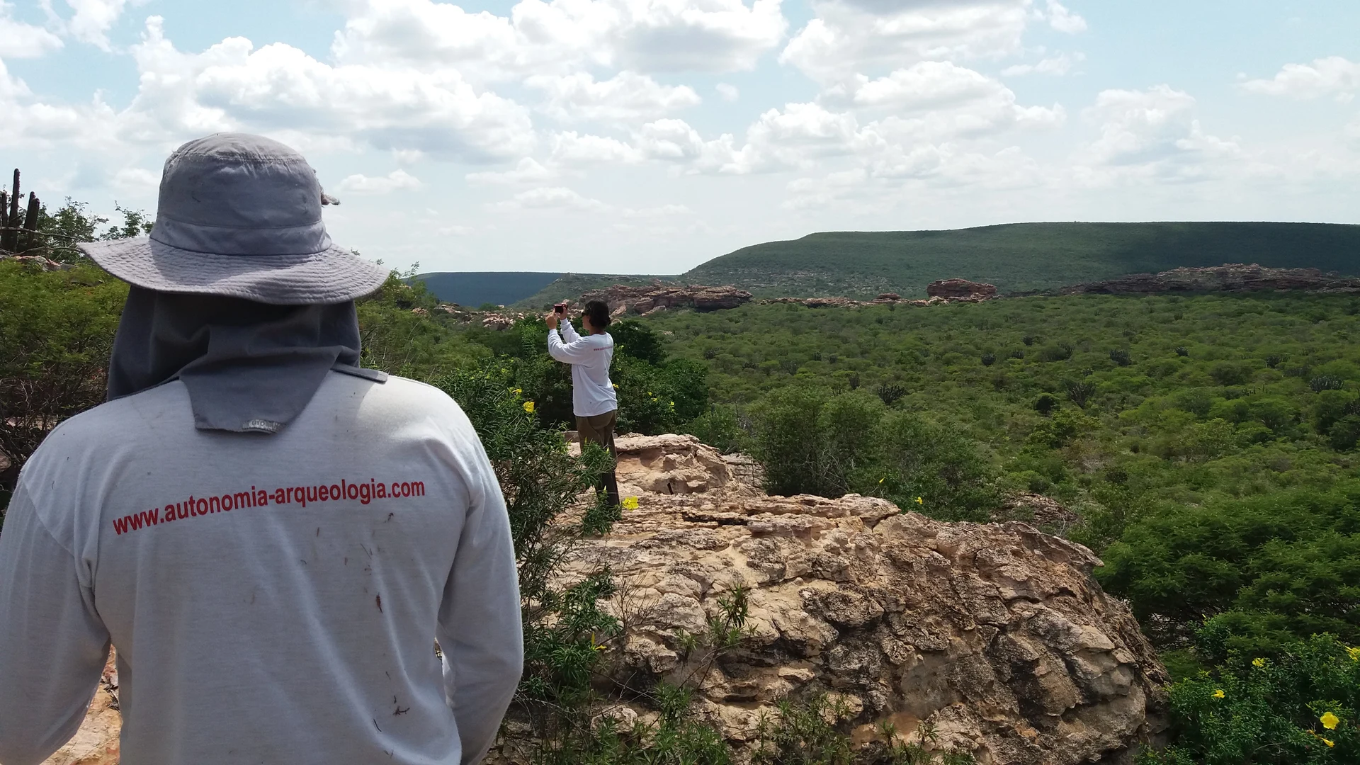 Autonomia Arqueologia: marca presente no trabalho de campo Profissional com camisa da Autonomia Arqueologia observa uma paisagem em atividade de campo.
