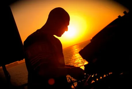 Silhueta de um DJ trabalhando diante do pôr do sol.