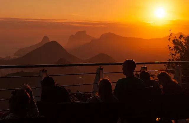 Pessoas contemplando o pôr do sol sobre as montanhas e a baía.
