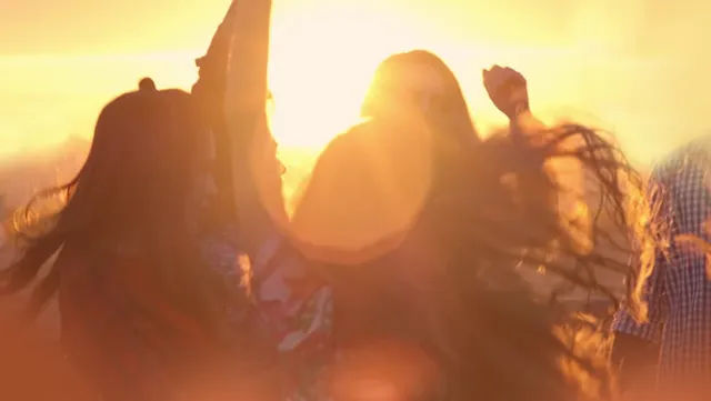 Pessoas dançando sob a luz dourada do sol.