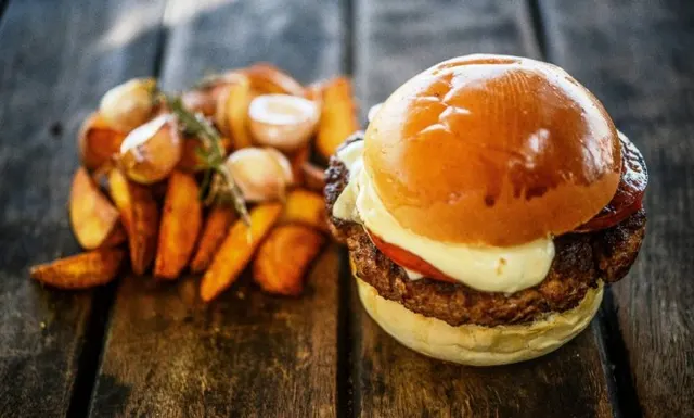 Hambúrguer servido com batatas e acompanhamentos.