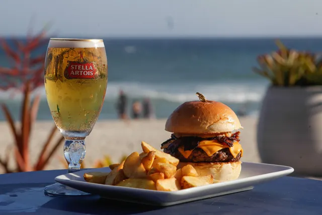Hambúrguer, batatas e uma taça de cerveja diante do mar.