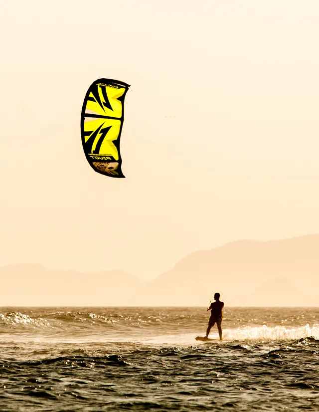Vela de kitesurf sobre a água na luz do entardecer.