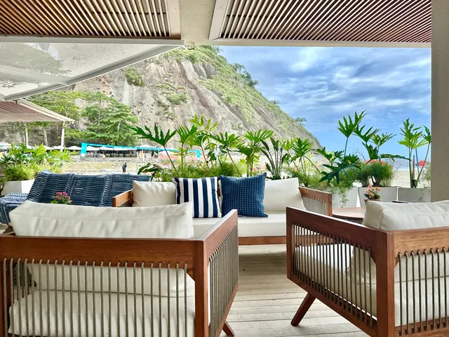 Lounge com poltronas, vegetação e vista para o morro junto à praia.