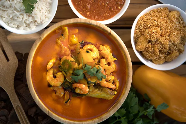 Moqueca servida em panela de barro com arroz e acompanhamentos.