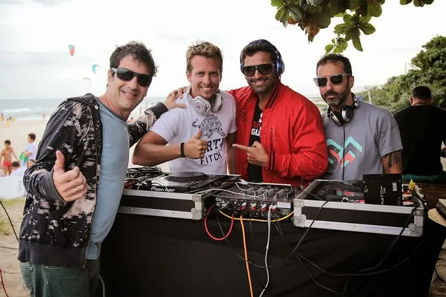 Grupo reunido ao lado de equipamentos de DJ em um encontro à beira-mar.