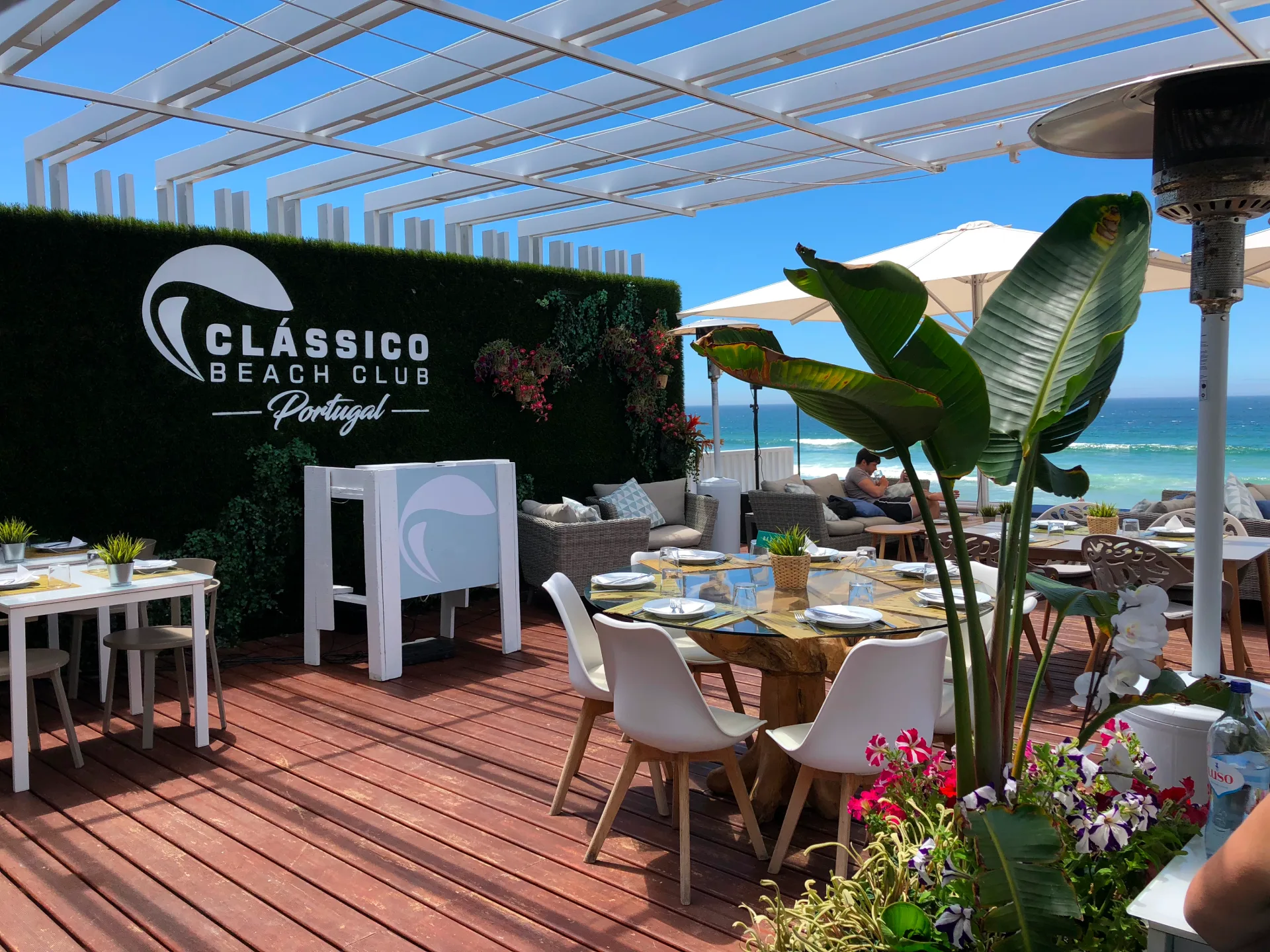 Terraço do Classico com mesas, plantas e vista para o mar.