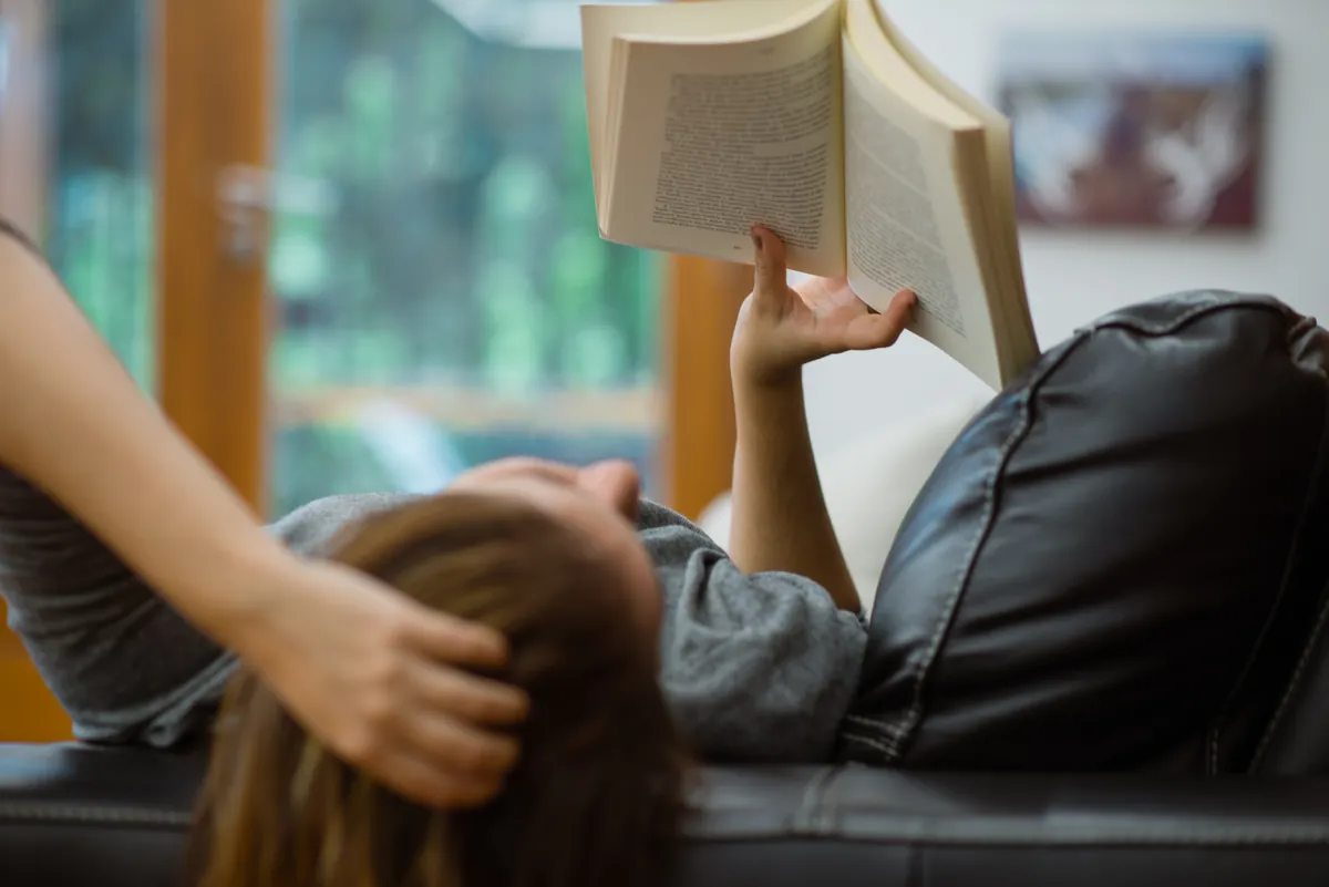 Mulher deitada em um sofá, lendo um livro.