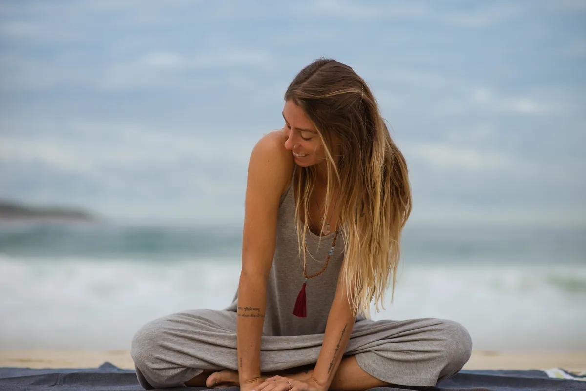Mulher sentada na areia da praia, de cabeça baixa.