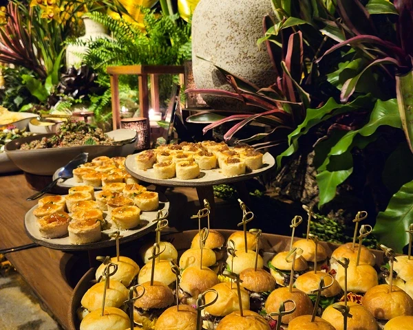 Buffet com pequenos pratos e ambientação tropical.