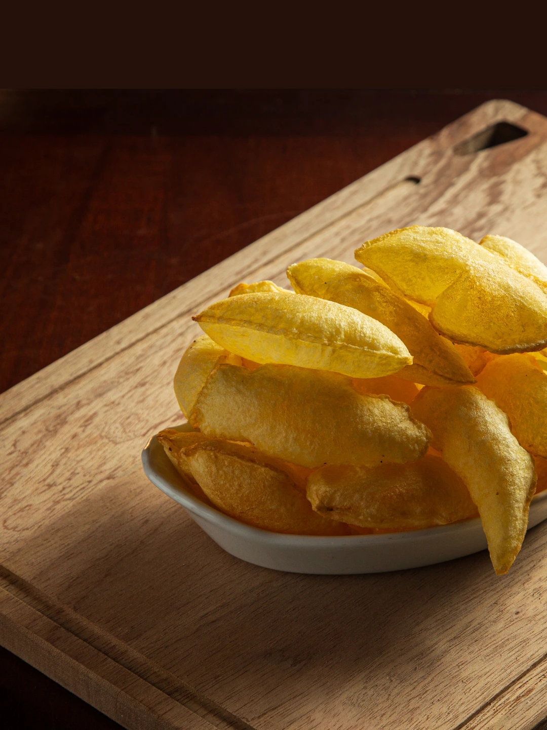 Porção de batatas douradas em recipiente branco sobre tábua de madeira.