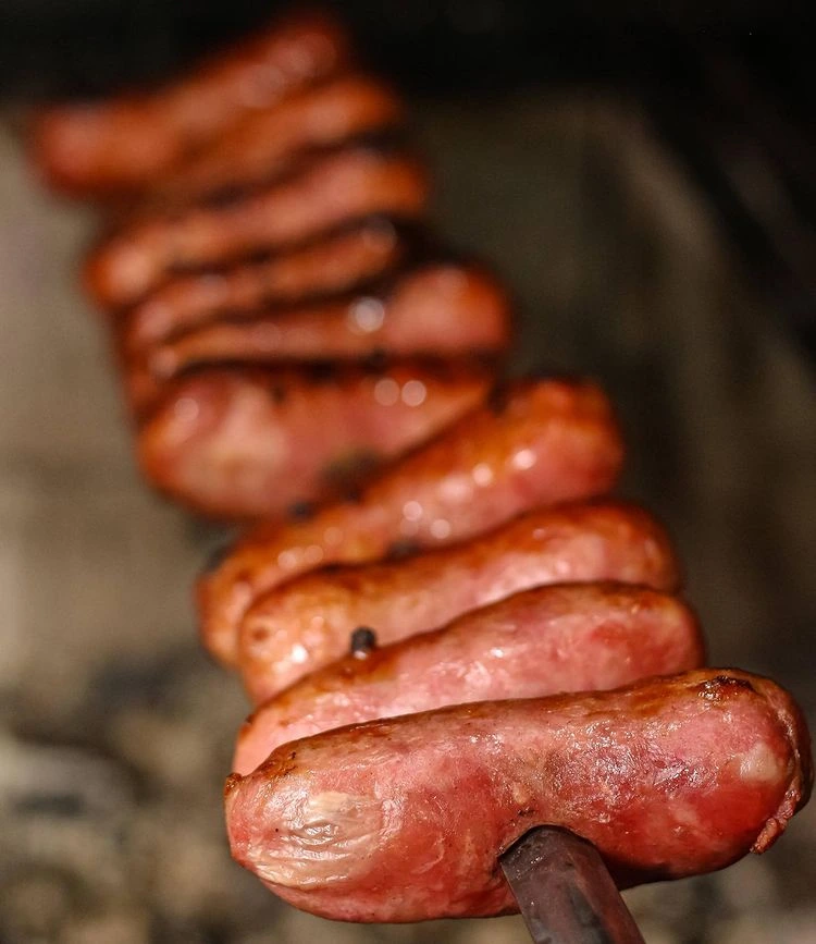 Linguiças douradas em espetos sobre a brasa.